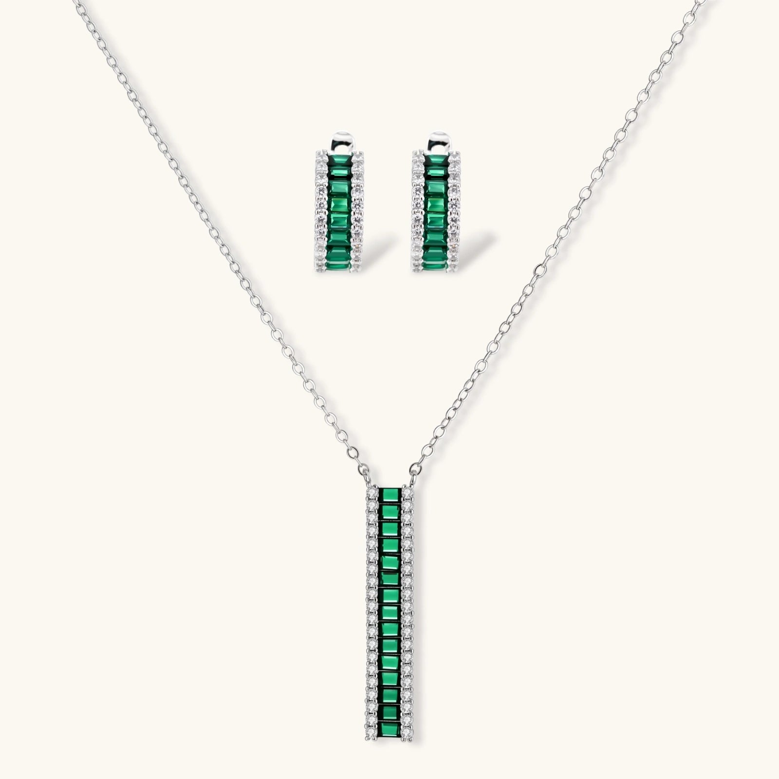White gold plated jewelry set with emerald green rectangular stones and clear crystals in geometric rows on white background.