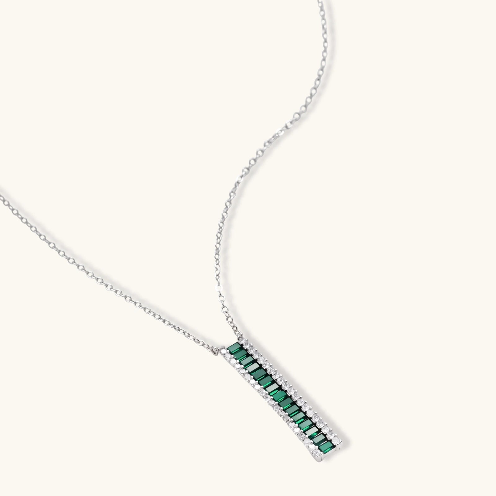 White gold plated jewelry set with emerald green rectangular stones and clear crystals in geometric rows on white background.