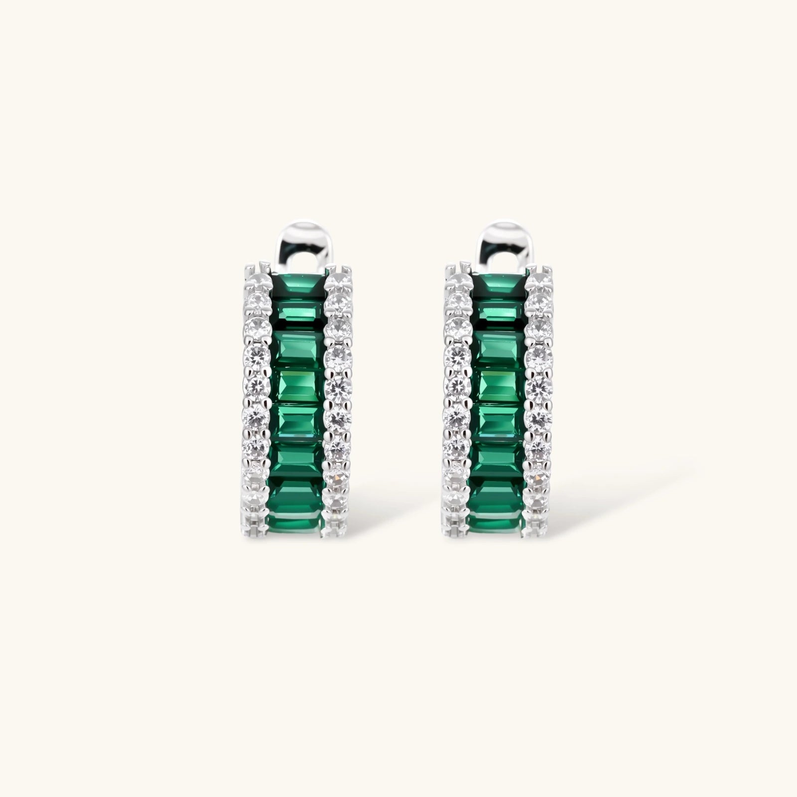 White gold plated jewelry set with emerald green rectangular stones and clear crystals in geometric rows on white background.
