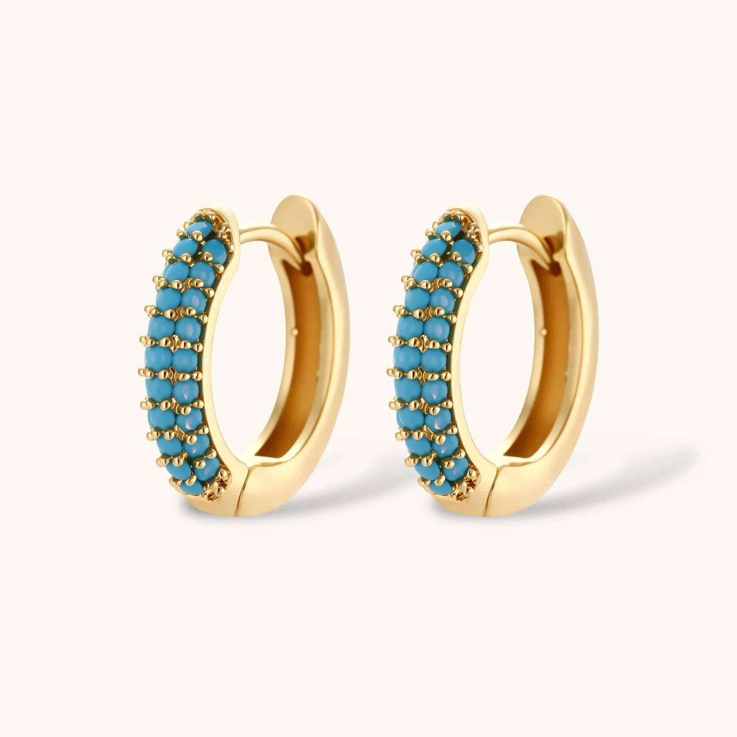 Gold-plated curved necklace and hoop earrings with turquoise cubic zirconia stones on white background.