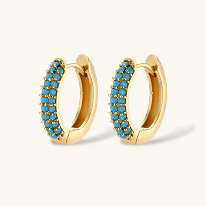 Gold-plated curved necklace and hoop earrings with turquoise cubic zirconia stones on white background.