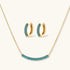Gold-plated curved necklace and hoop earrings with turquoise cubic zirconia stones on white background.