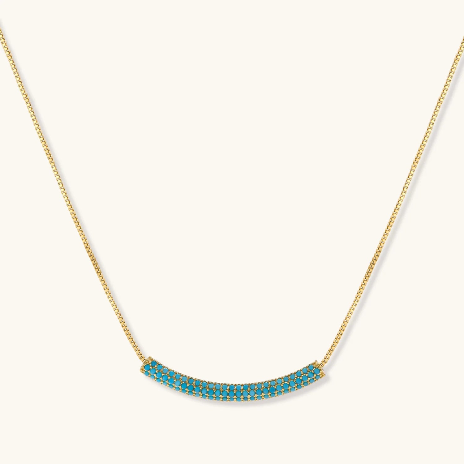 Gold-plated curved necklace and hoop earrings with turquoise cubic zirconia stones on white background.