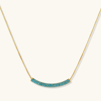Gold-plated curved necklace and hoop earrings with turquoise cubic zirconia stones on white background.