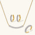 Gold-plated curved necklace, hoop earrings, and adjustable ring with pavé cubic zirconia stones on cream background.