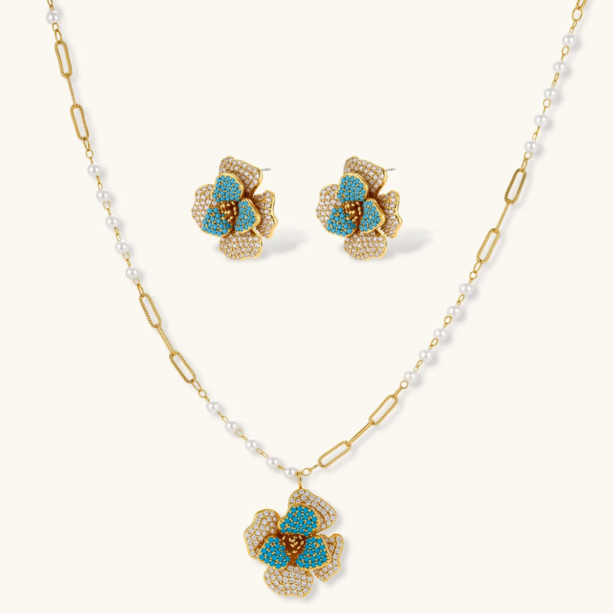 14K gold-plated floral jewelry set with blue cubic zirconia centers and pearl chain details on white background.