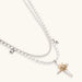 Two-layer silver-toned necklace with star charms and dagger pendant featuring golden sun motif on white background.