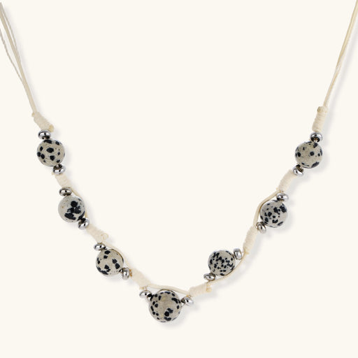 Adjustable cream cord necklace with white spotted stone beads featuring black speckles on neutral background