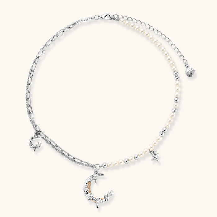 Silver-toned crescent moon pendant with star accents on pearl and chain necklace against white background.