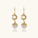 Gold sunburst charm earrings with baroque pearl drops on French hooks against cream background