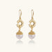 Gold sunburst charm earrings with baroque pearl drops on French hooks against cream background