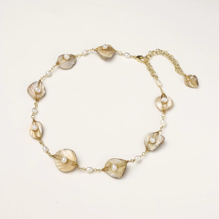 Gold-plated necklace with wire-wrapped shell pieces and freshwater pearls on neutral background, adjustable chain visible.