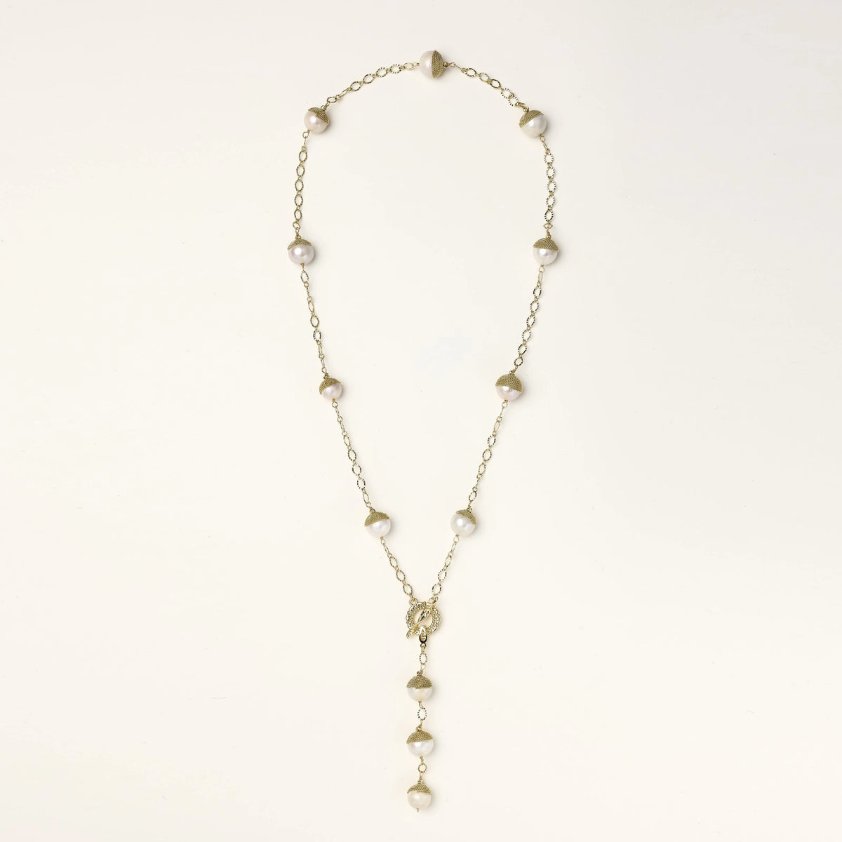 Gold-plated lariat necklace with baroque pearls and textured caps on cream background, showing adjustable Y-shaped design.