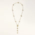 Gold-plated lariat necklace with baroque pearls and textured caps on cream background, showing adjustable Y-shaped design.