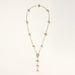 Gold-plated lariat necklace with baroque pearls and textured caps on cream background, showing adjustable Y-shaped design.