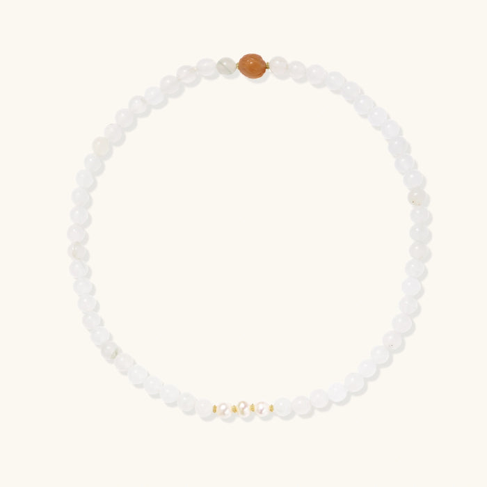 Three layered white beaded bracelets with carved orange agate lotus centerpiece and freshwater pearls on cream background.