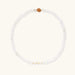 Three layered white beaded bracelets with carved orange agate lotus centerpiece and freshwater pearls on cream background.