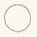 Delicate necklace with black blue sandstone beads and baroque pearl center on white background with gold accents.
