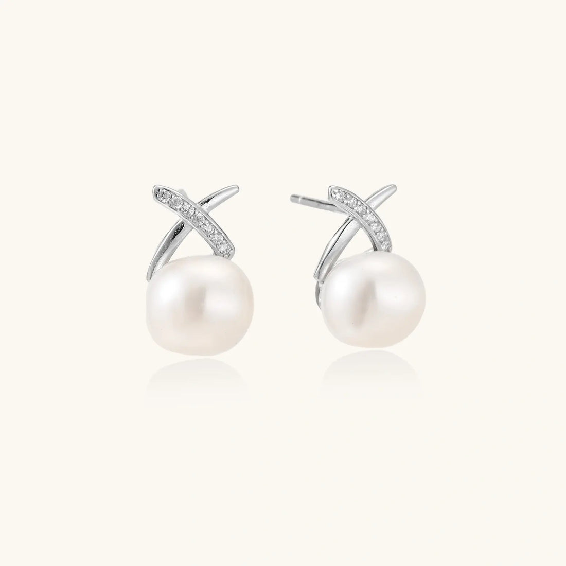 Rhodium-plated silver stud earrings with sparkling X design above lustrous round freshwater pearls on white background.