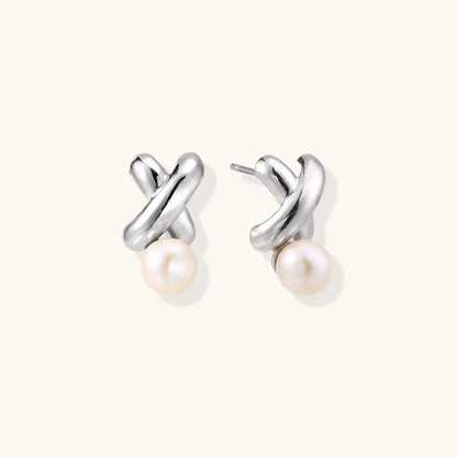 Rhodium-plated silver earrings with twisted X design and freshwater pearl drops on beige background