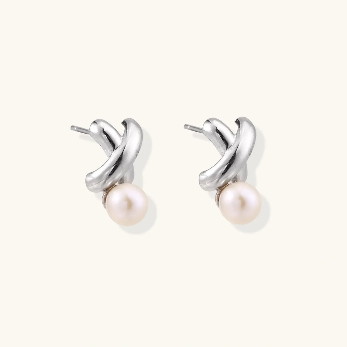 Rhodium-plated silver earrings with twisted X design and freshwater pearl drops on beige background