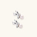 Rhodium-plated silver earrings with twisted X design and freshwater pearl drops on beige background