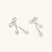 Rhodium-plated silver earrings with organic vine curves and two peachy freshwater pearls on cream background