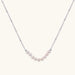Delicate sterling silver chain necklace with small freshwater pearls arranged in a curved smile arc on cream background.