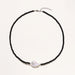 Beaded black agate necklace with iridescent baroque freshwater pearl centerpiece on cream background.