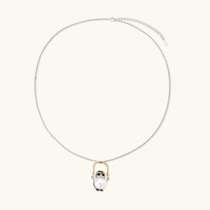Whimsical owl pendant holding a white pearl on a gold swing, rhodium-plated silver chain on cream background.