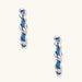 White gold-plated hoops intertwined with blue denim fabric in a twisted rope design on cream background.