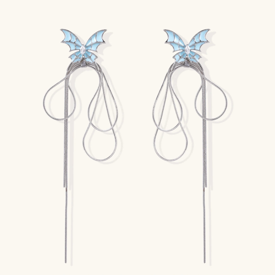 Long silver-tone earrings with powder blue enamel butterfly studs and flowing chain tassels on cream background