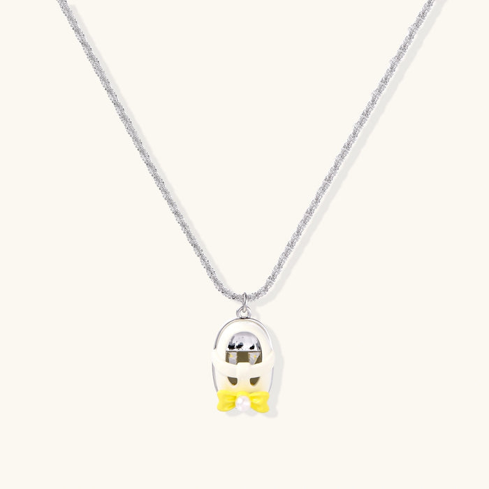 Chrome egg-shaped pendant with kawaii face, yellow bow, and pearl detail on silver chain against white background