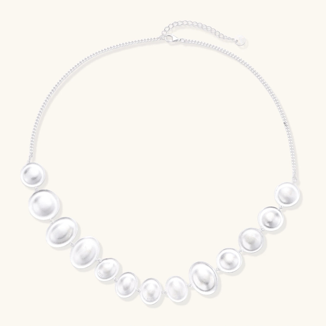 Graduated pearl-finish silver discs forming an organic bubble bib necklace on delicate chain against cream background.
