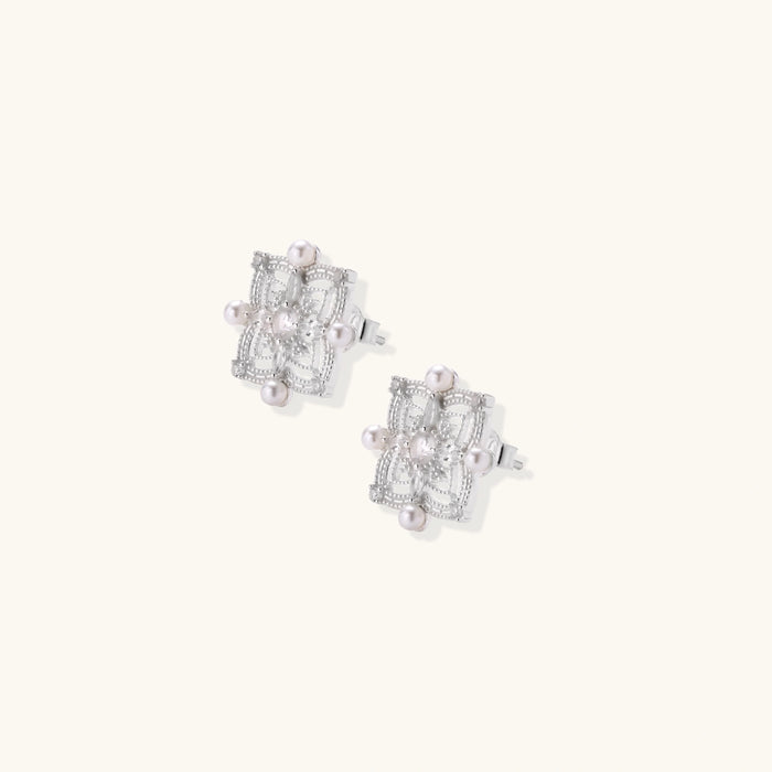 Ornate sterling silver stud earrings with mandala-inspired filigree pattern and four freshwater pearls on beige background