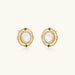Circular gold stud earrings with iridescent mother-of-pearl center and green zirconia accents on cream background.
