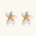 White enamel tropical flower earrings with sculptural gold-plated center and organic petal design on cream background