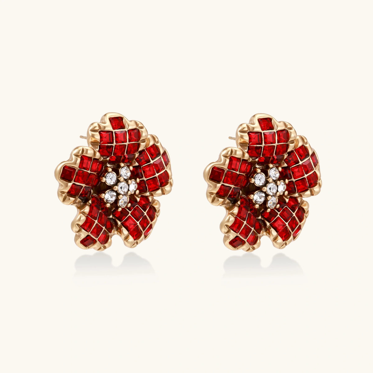 Gold-plated flower studs with burgundy square crystals in petal mosaic and clear center stones on beige background.