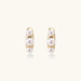 14K gold-plated curved stud earrings with three white freshwater pearls aligned vertically on cream background