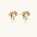 Gold-plated flower stud earrings with textured petals and centered freshwater pearl on beige background
