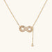 Gold infinity pendant with baguette crystals on adjustable chain against cream background.