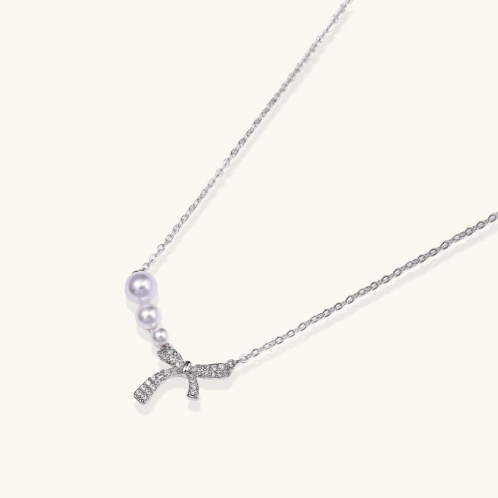 Delicate white gold plated necklace with freshwater pearls and sparkly crystal bow pendant on white background