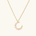 Gold crescent moon pendant with graduated white pearls on delicate chain against cream background