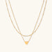 Delicate double-chain gold necklace with tiny heart pendant on cream background