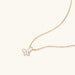 Gold-plated butterfly pendant with iridescent mother of pearl inlay on delicate chain against cream background.