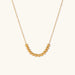 Delicate gold-plated necklace with graduated spherical beads forming gentle smile curve on beige background