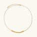 Delicate gold-plated necklace with graduated spherical beads forming gentle smile curve on beige background