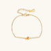 Delicate gold chain bracelet with minimalist bar and centered knot detail on cream background