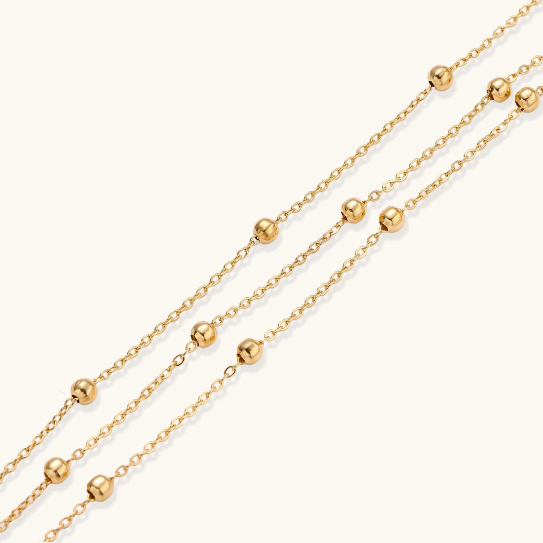Three-strand gold-plated bracelet with clustered ball beads and adjustable clasp on cream background