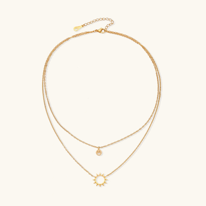 Gold layered necklace set with sunburst and smiley face pendants on delicate chains against white background.